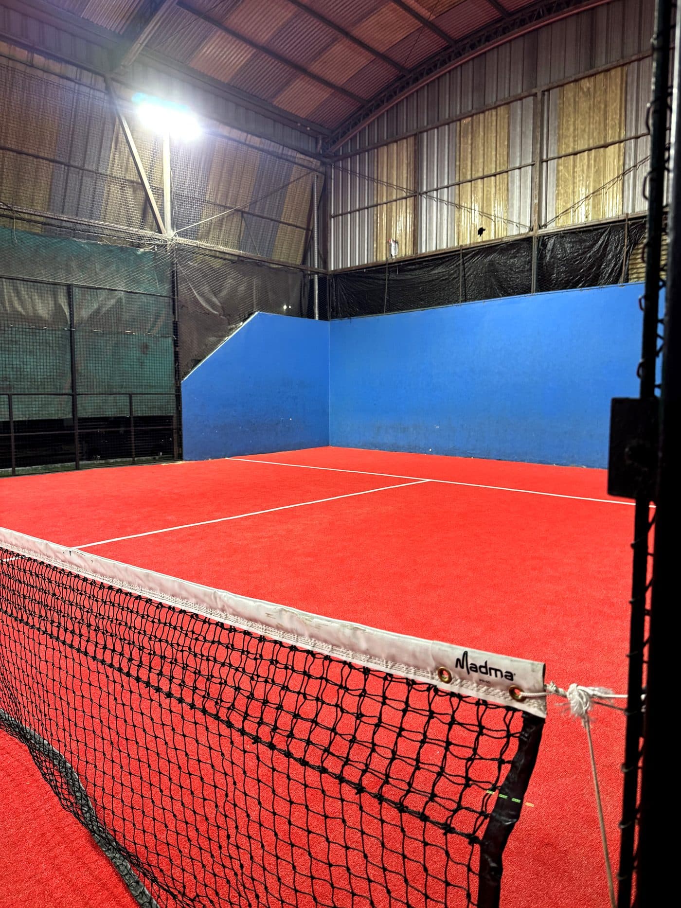 Una de las canchas de pádel de noche, con el piso rojo y la pared del fondo azul.